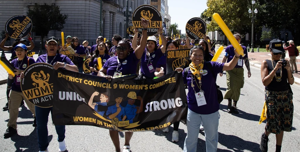 District Council 9 Women’s Committee members marching with a banner that reads 'Union Women Strong' during a labor rally supporting women in the trades