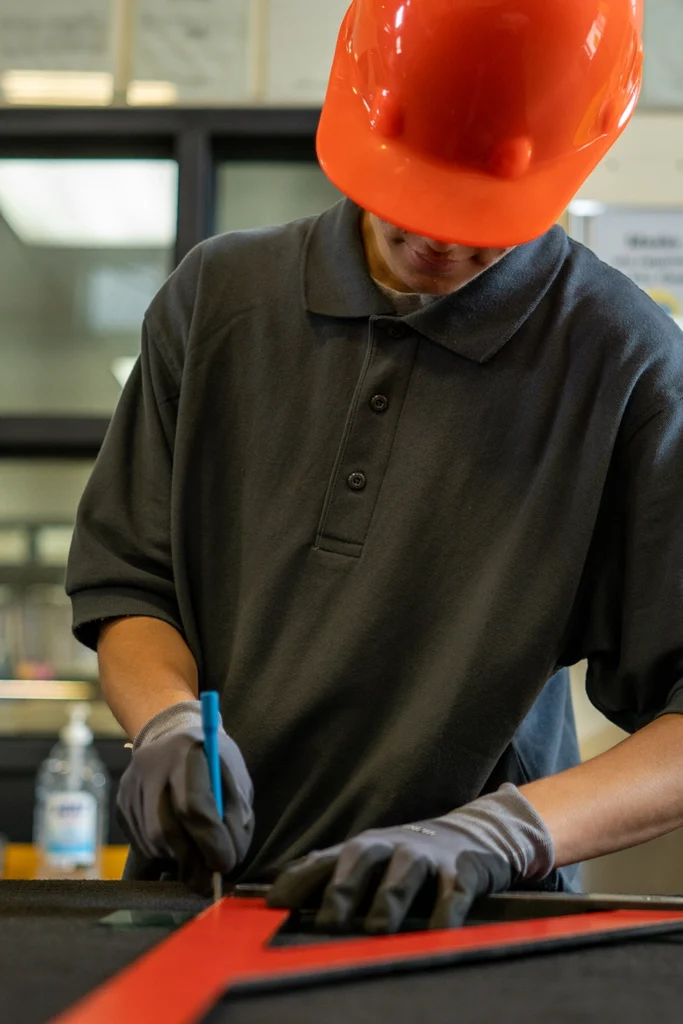 Skilled trades apprentice in orange hard hat using a cutting tool in a training workshop